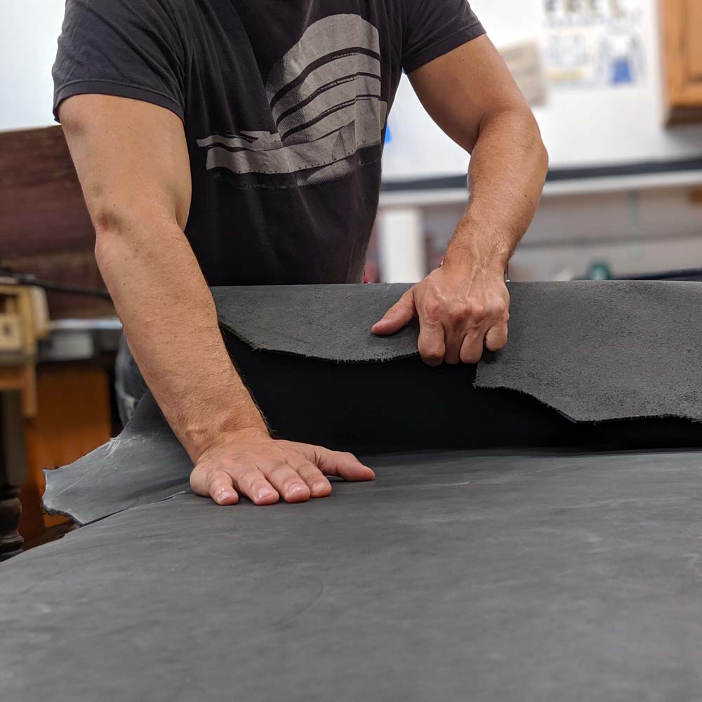 Person unrolling a hide of full-grain leather on a workbench.